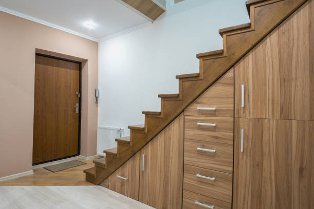 Modern architecture interior with luxury hallway with glossy wooden stairs in multi-storey house. Custom built pullout cabinets on glides in slots under stairs. Use of space for storage.